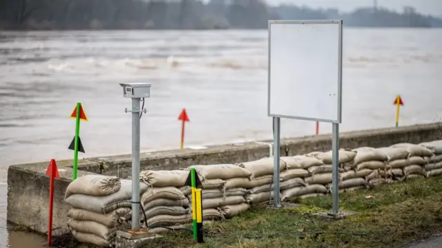 Pegel am Fluss mit Sandsäcken und Warnmarkierungen bei Hochwasser-Warnstufen