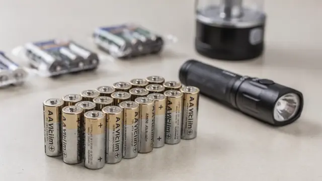 AA- und AAA-Batterien neben einer Taschenlampe und einer kleinen Laterne auf einem Tisch